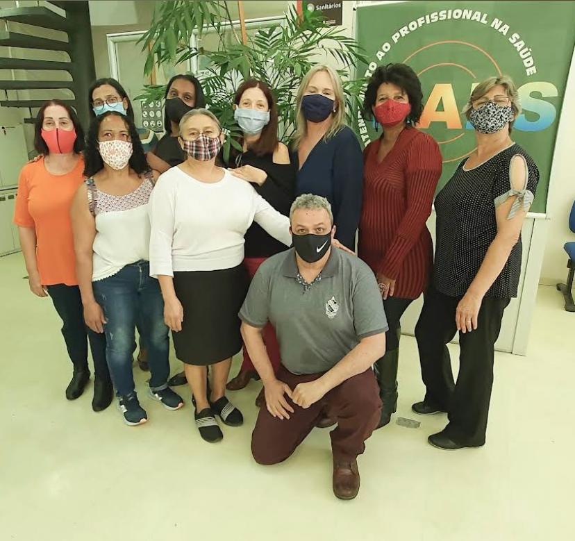 David está agachado e atrás dele há nove mulheres em pé. Ao fundo das mulheres há uma planta grande.